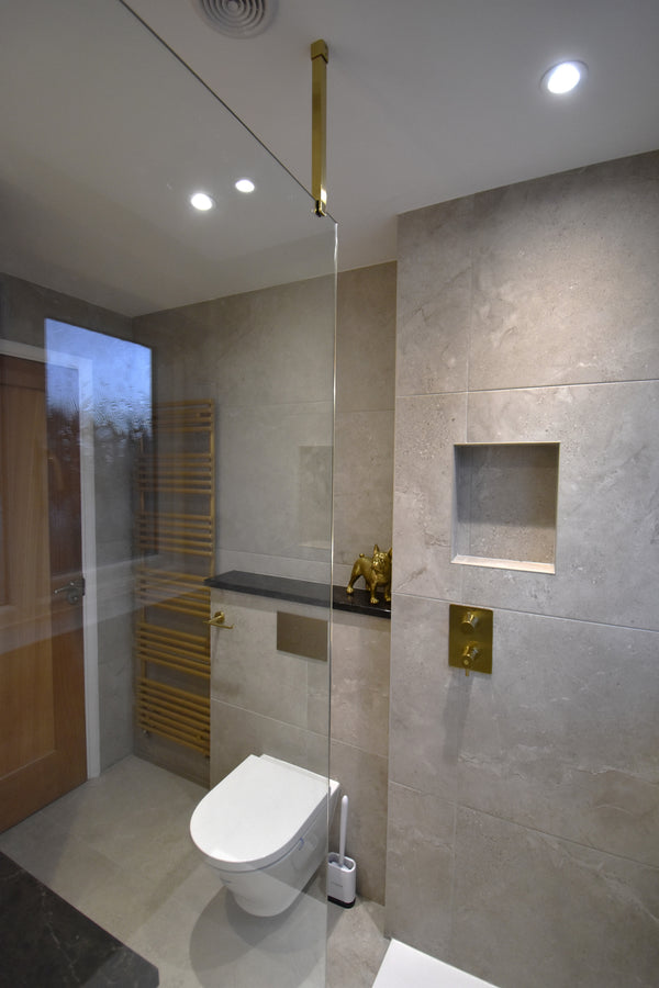Modern bathroom interior with large light beige stone tiles, a white toilet and a gold wall-mounted fixture.